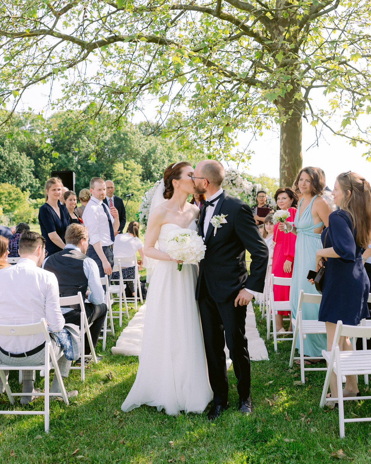 Bride and groom kiss during an outdoor garden ceremony with their guests