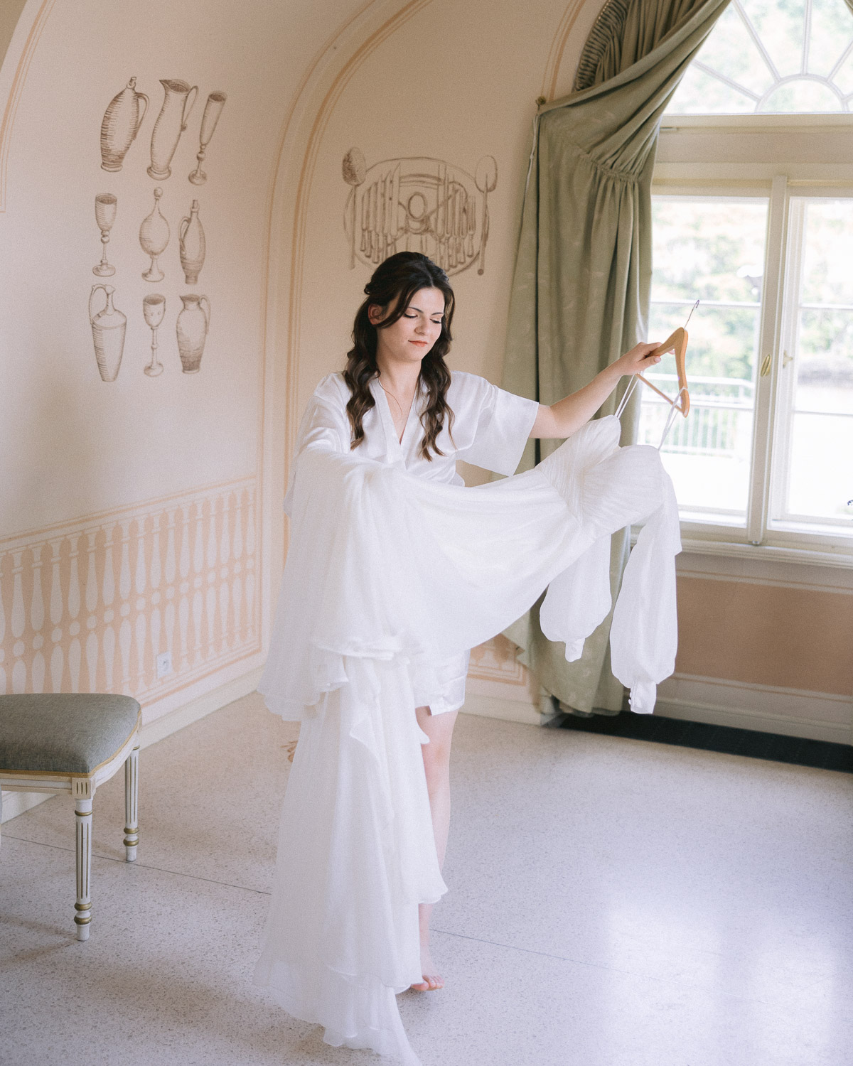 Bride putting on her dress by the window