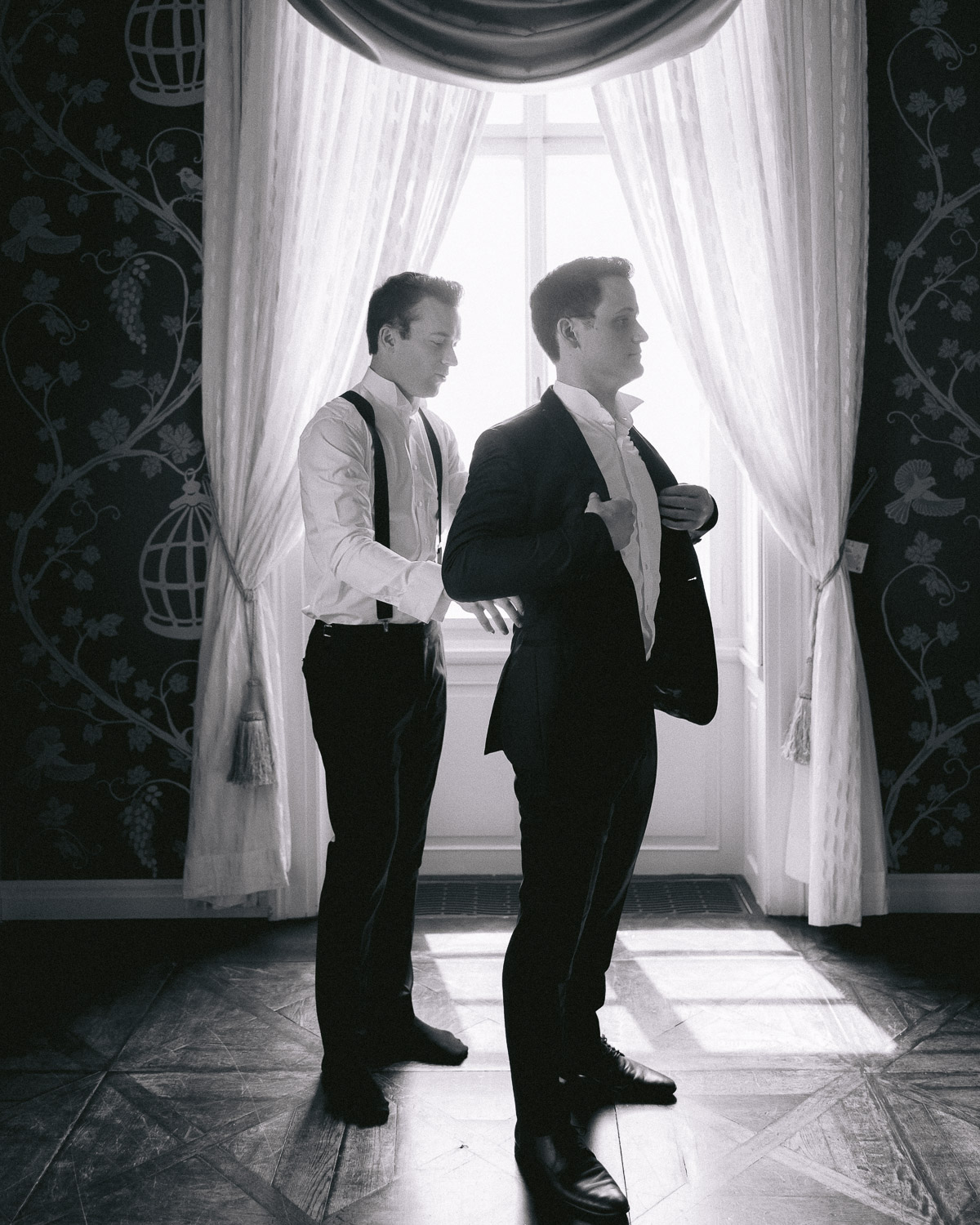 Groom and groomsman getting ready by the window, black and white