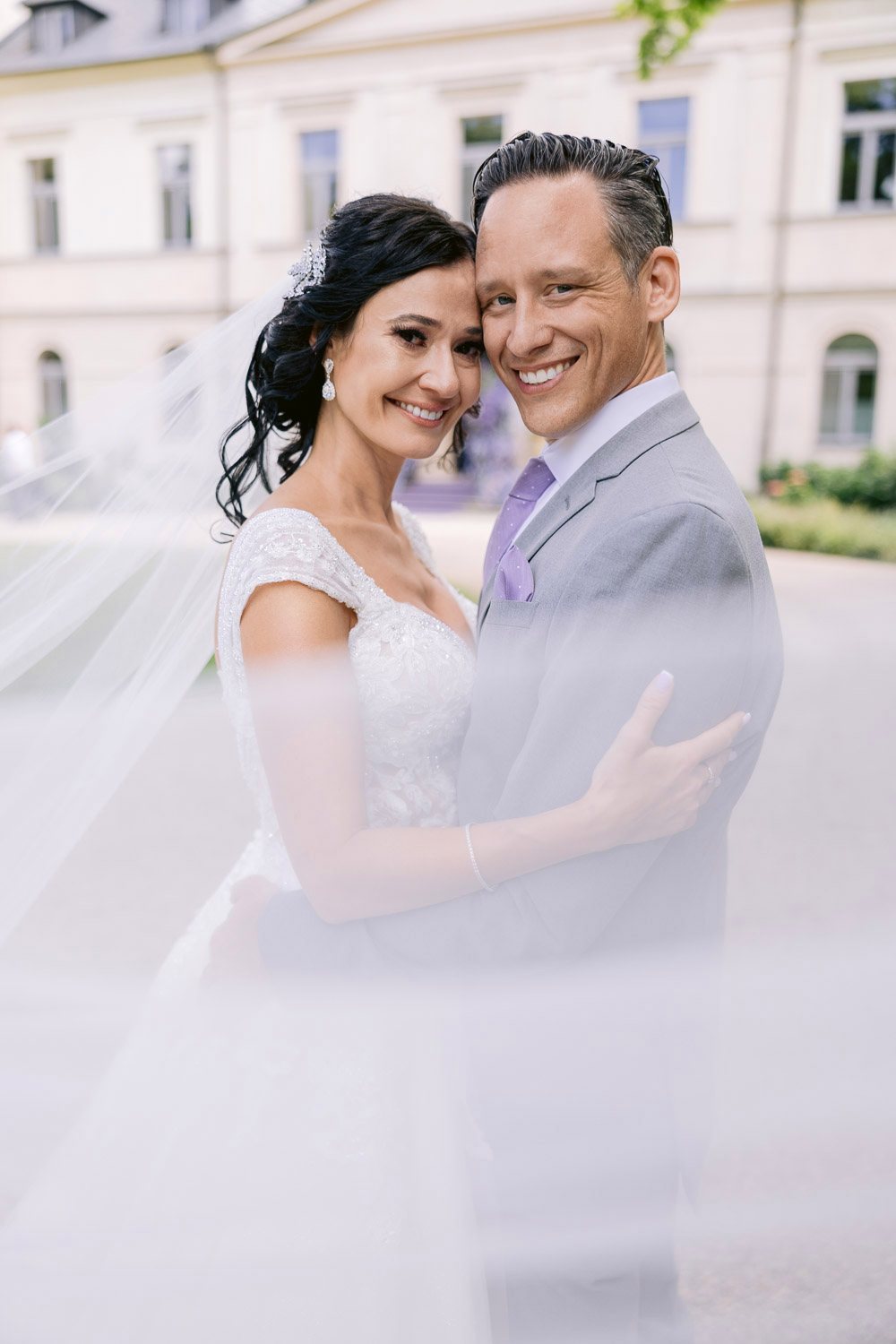 Chateau Mcely Bride Veil Portrait Bride and groom wrapped in her veil in front of the château