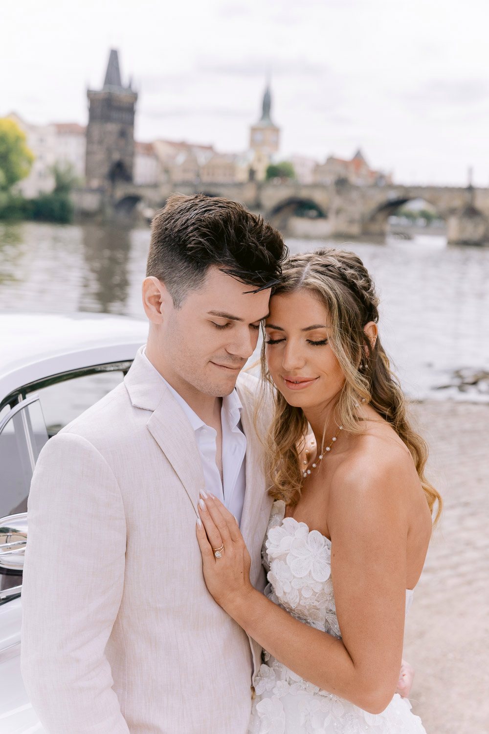 Lobkowicz Palace Elopement Couple Embrace Charles Bridge Couple embracing on the Vltava bank with Charles Bridge behind