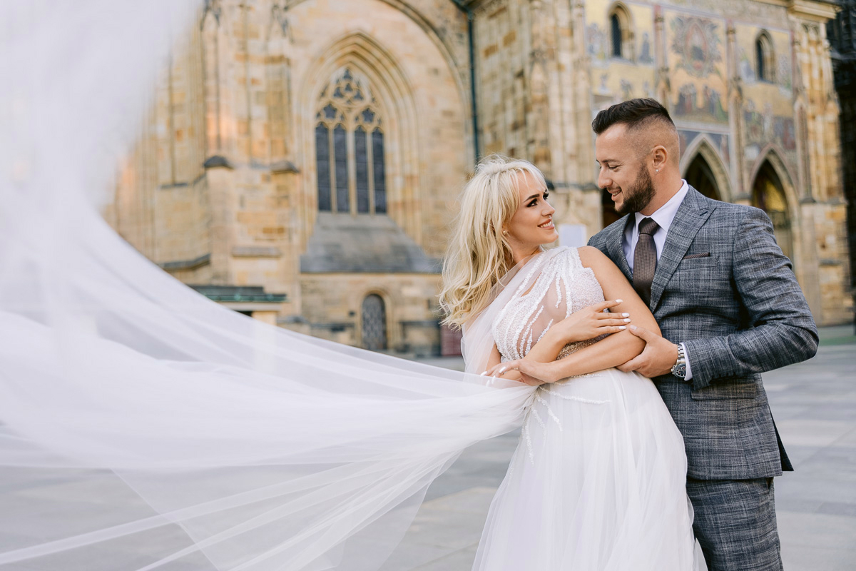 Bride and groom in front of St. Vitus Cathedral at Prague Castle, her veil flowing in the wind