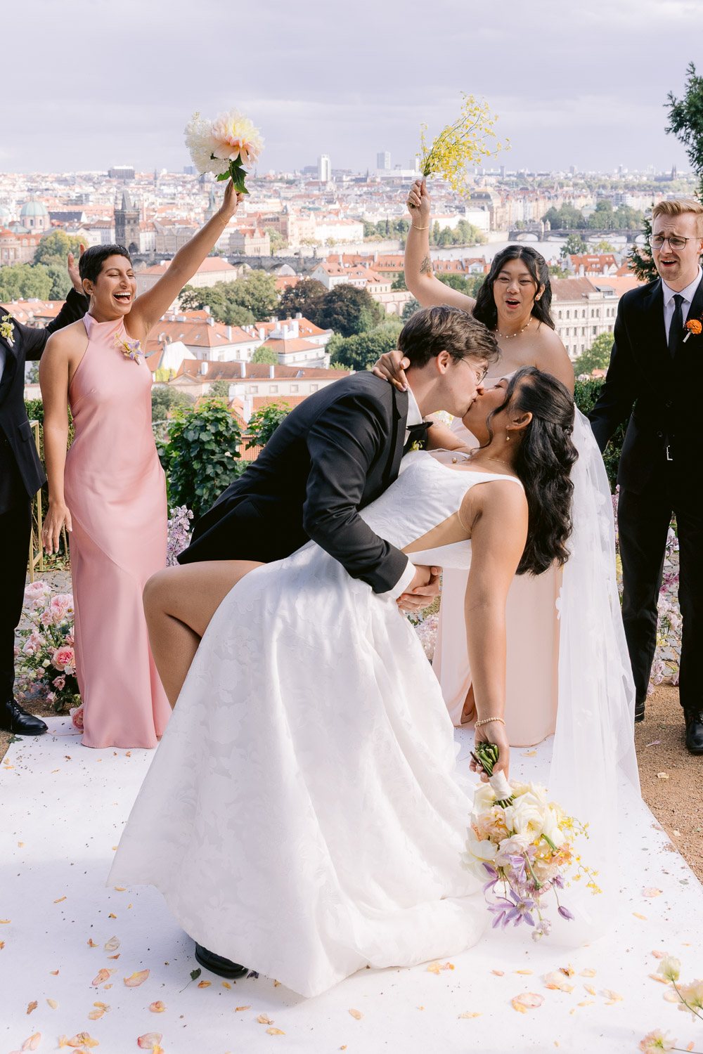 Villa Richter Wedding Kiss Dip Prague View Groom dipping the bride for a kiss at the end of the ceremony at Villa Richter as bridesmaids cheer, with Prague behind them